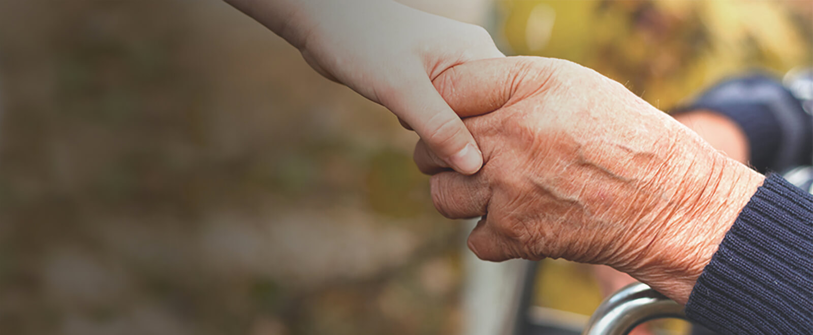 Young person hand reaching down to hold the hand of an elderly person