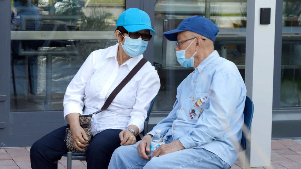 Des gens assis dehors portant des couvres-visage