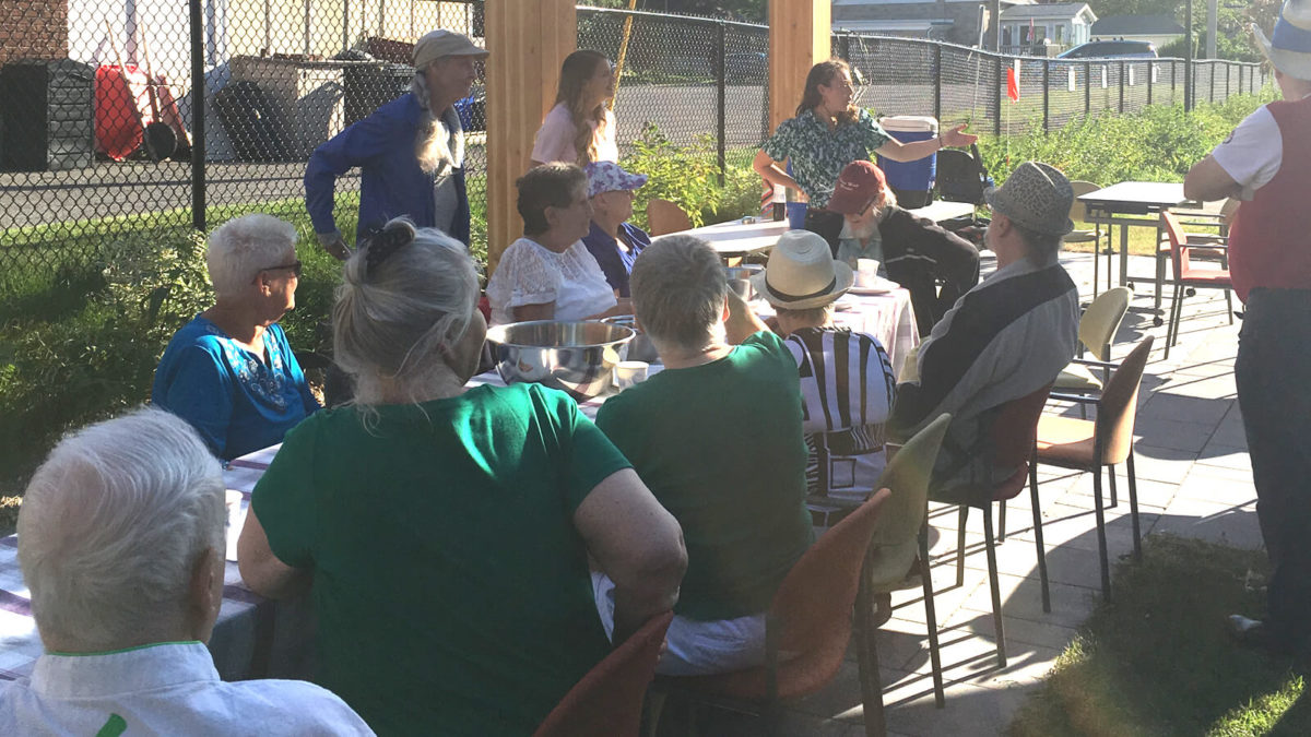 Group of people seated around an outdoor table, listening to presentation