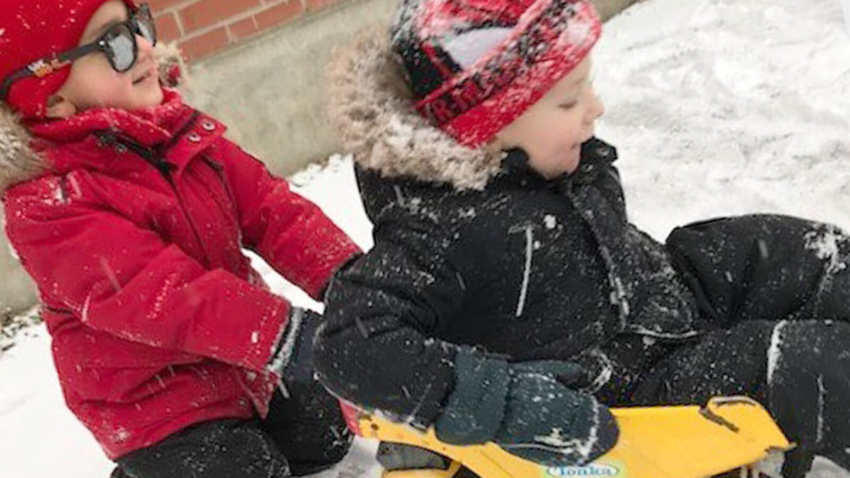 Two children playing outside in the snow with a toy truck