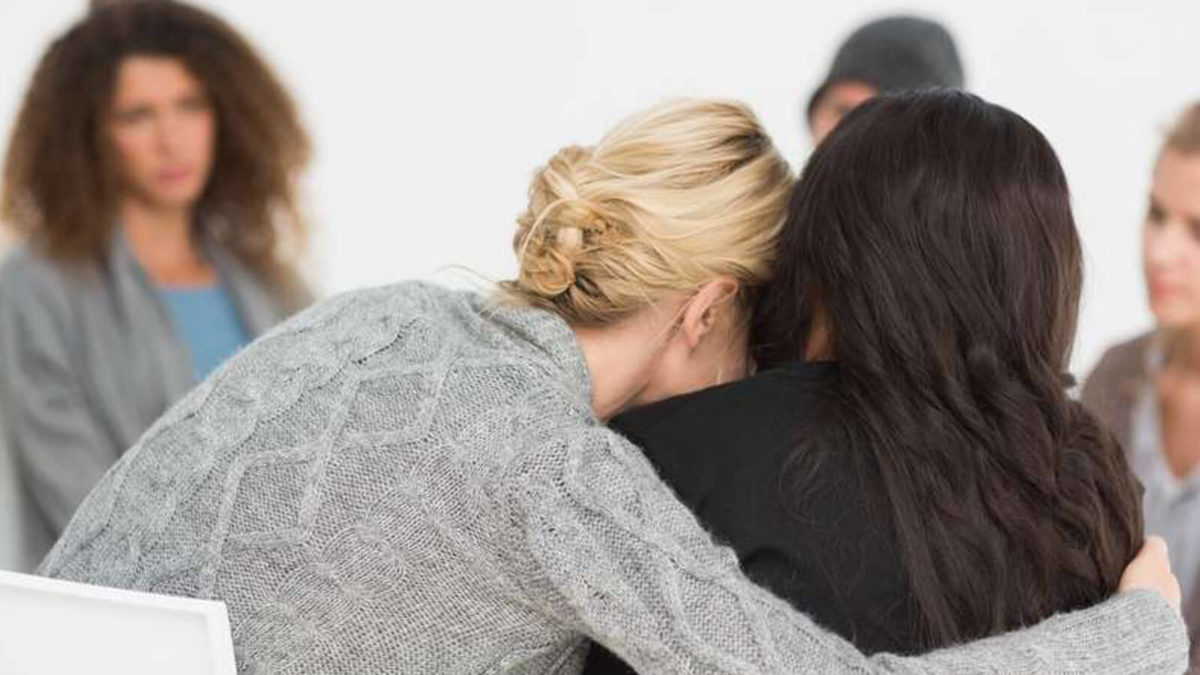 A woman hugging another woman in a group counselling session